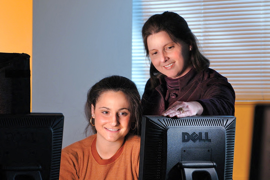 instructor and student smiling while looking at a computer screen