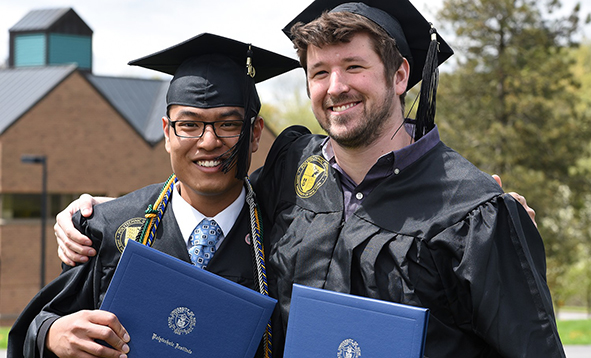 two male students with graduation cap and gown holding diplomas
