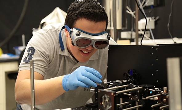 student in a lab wearing goggles with a tool