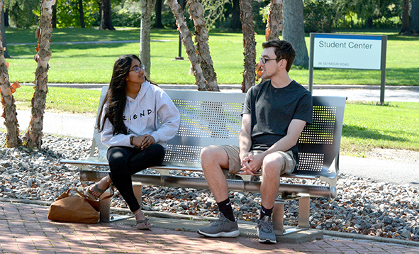 Two college students sitting on a bench on a sunny day
